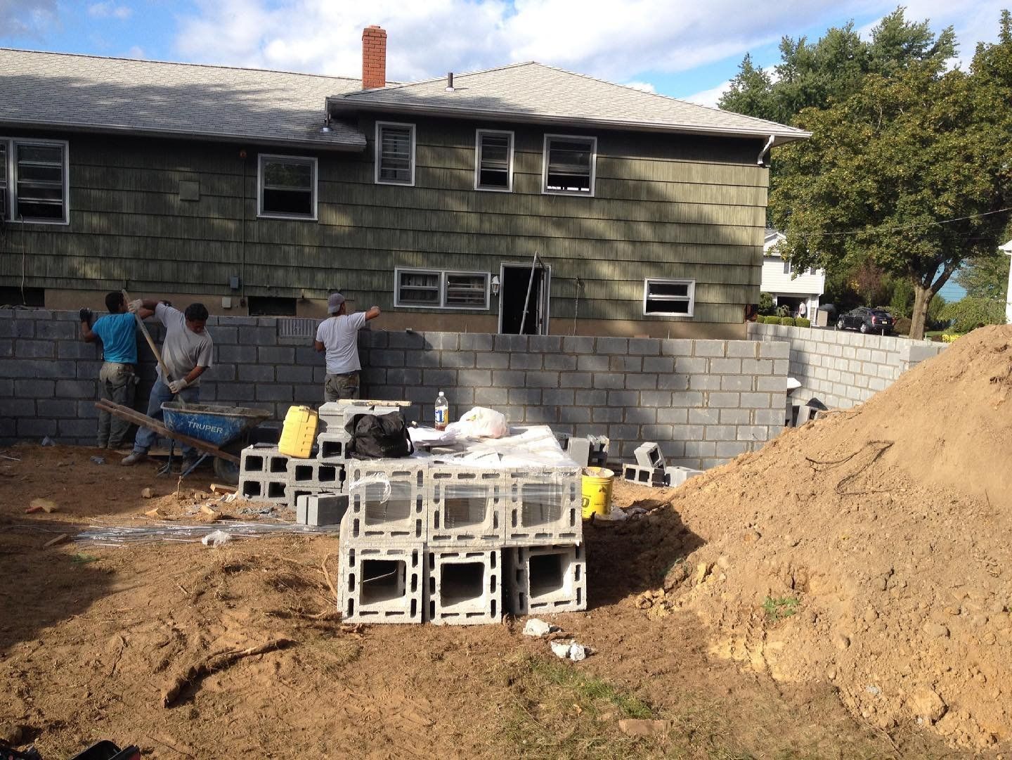 Crew laying a concrete block foundation wall beside an existing home at the start of an addition