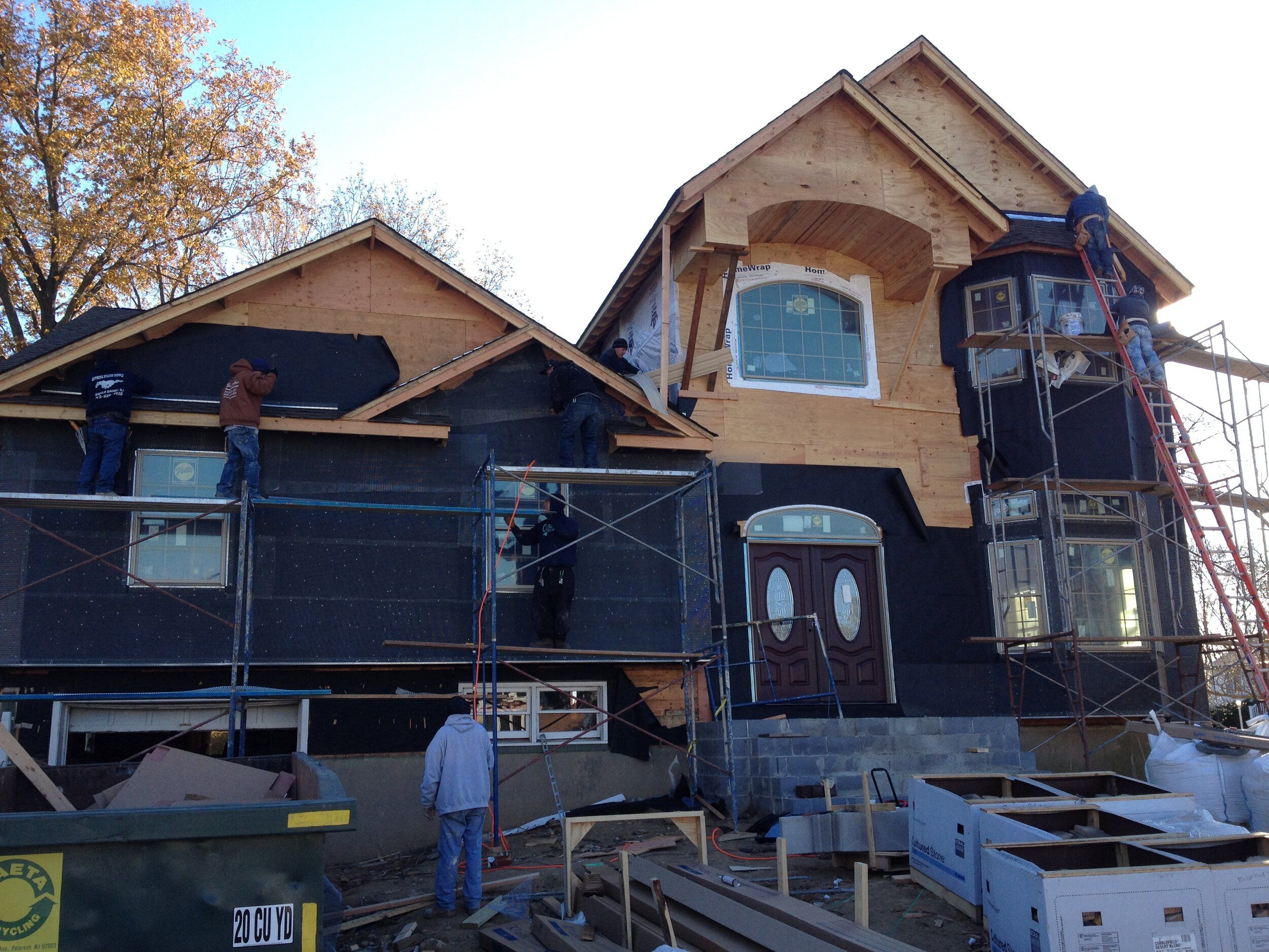 Exterior of a New Jersey home being built with weather barrier and framing while workers and scaffolding are on site
