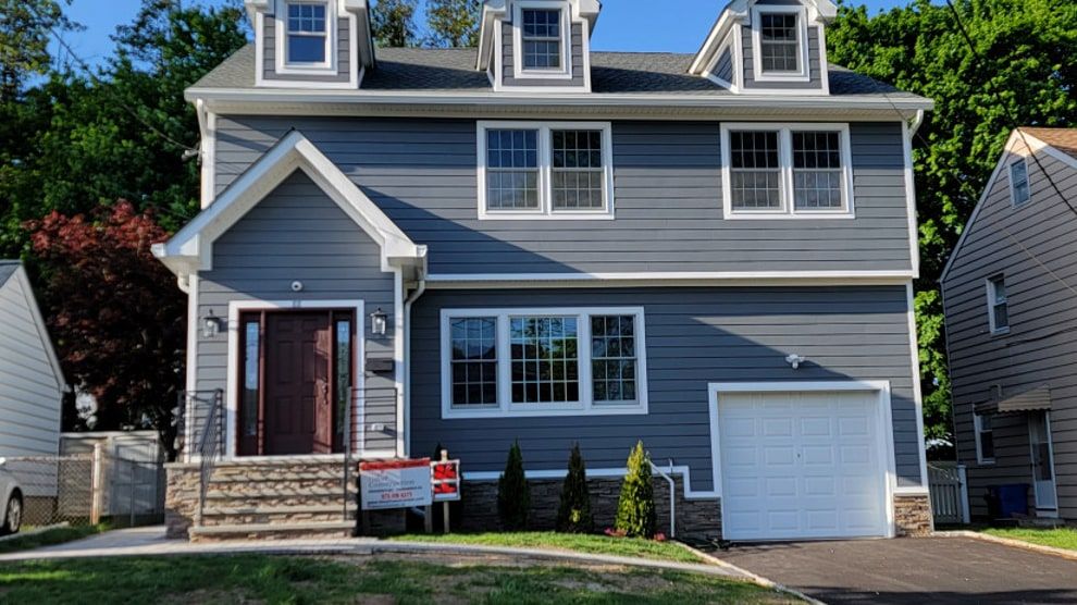 A Nutley, NJ home after a total renovation by Omar Construction, with gray siding, three dormers and a new front entry