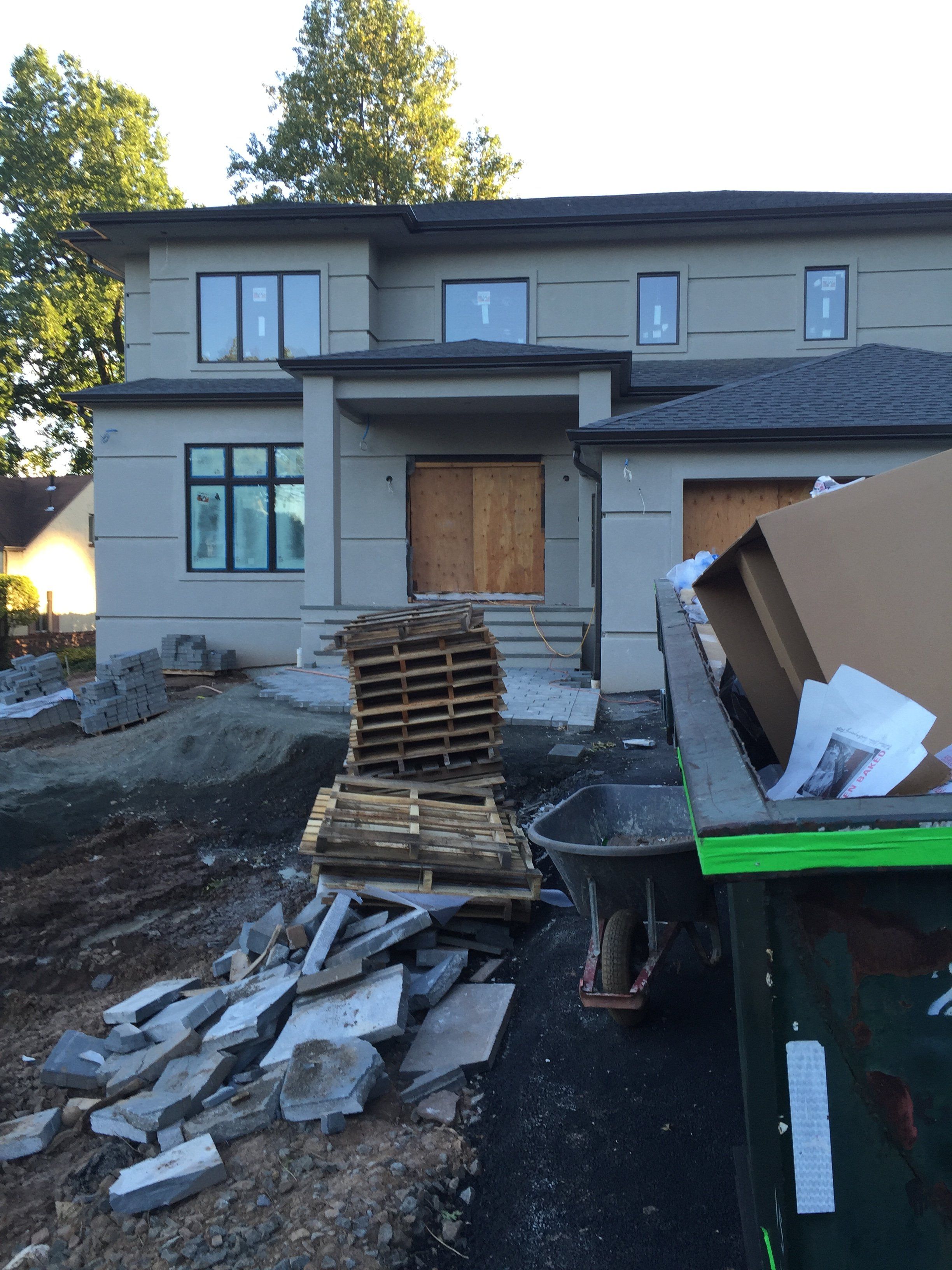 Two-story stucco and stone home under construction in New Jersey, with building materials and a dumpster in front