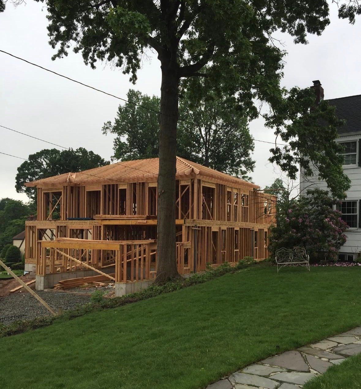 Wood framing of a new two-story house in Passaic Park, NJ beside a large tree