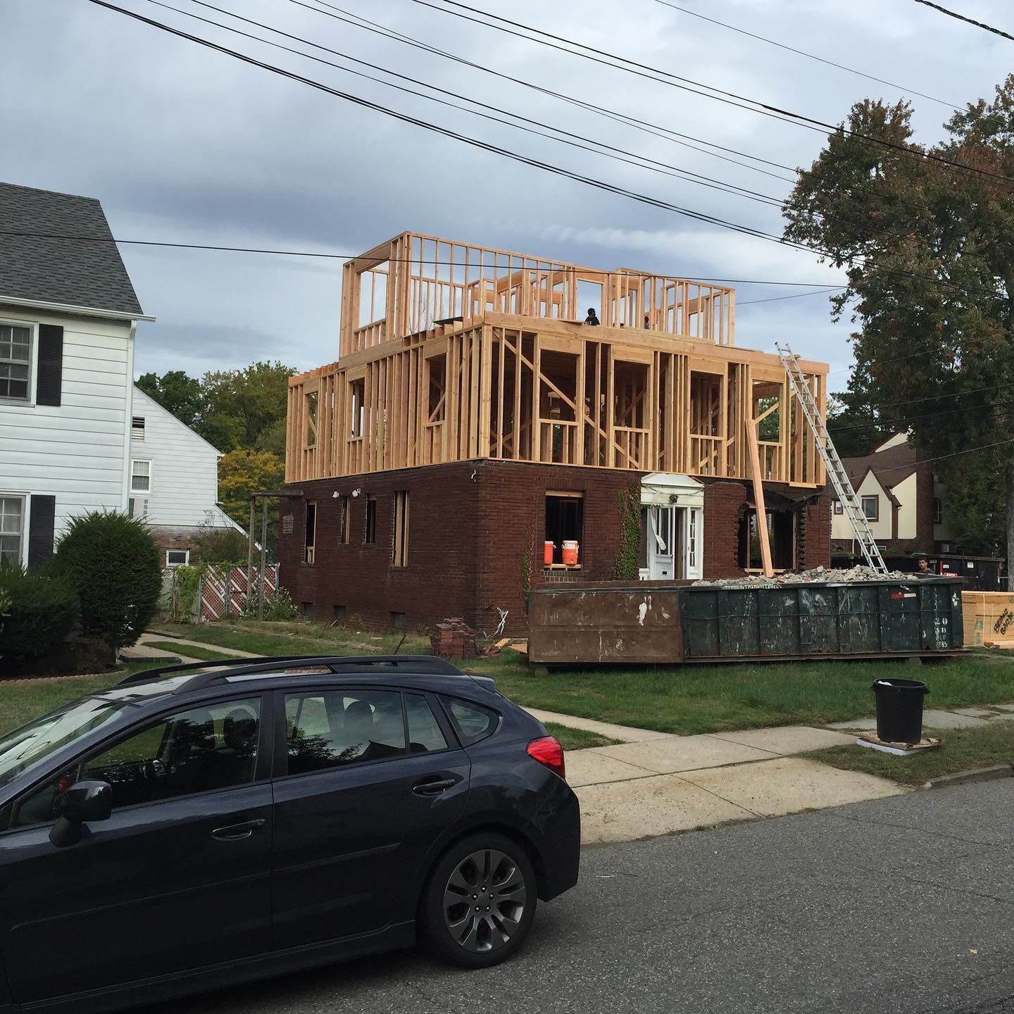 Second-story addition being framed on top of a brick house, with a dumpster out front