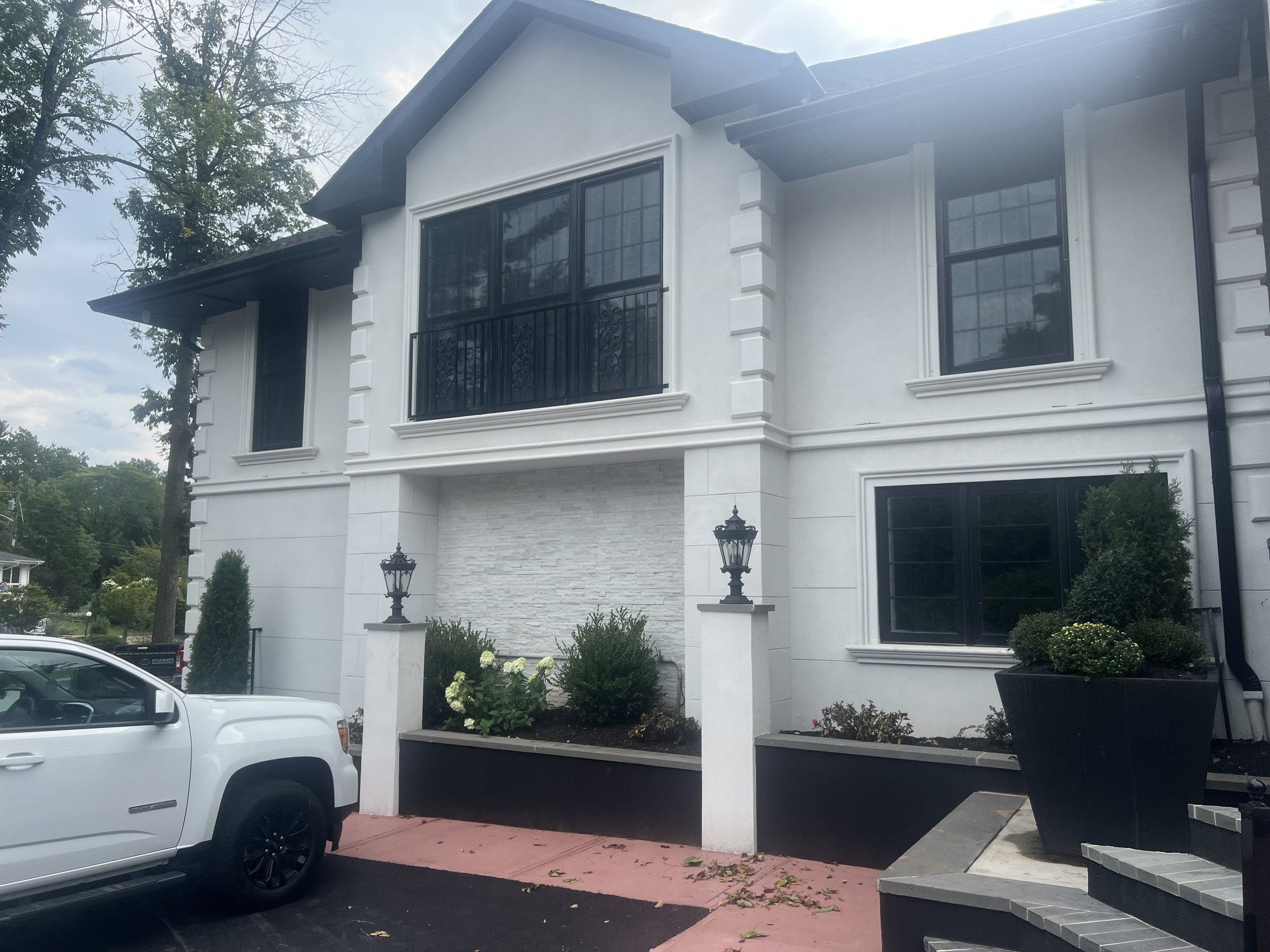 White stucco two-story home with black windows, stone details and a landscaped entry, built by Omar Construction